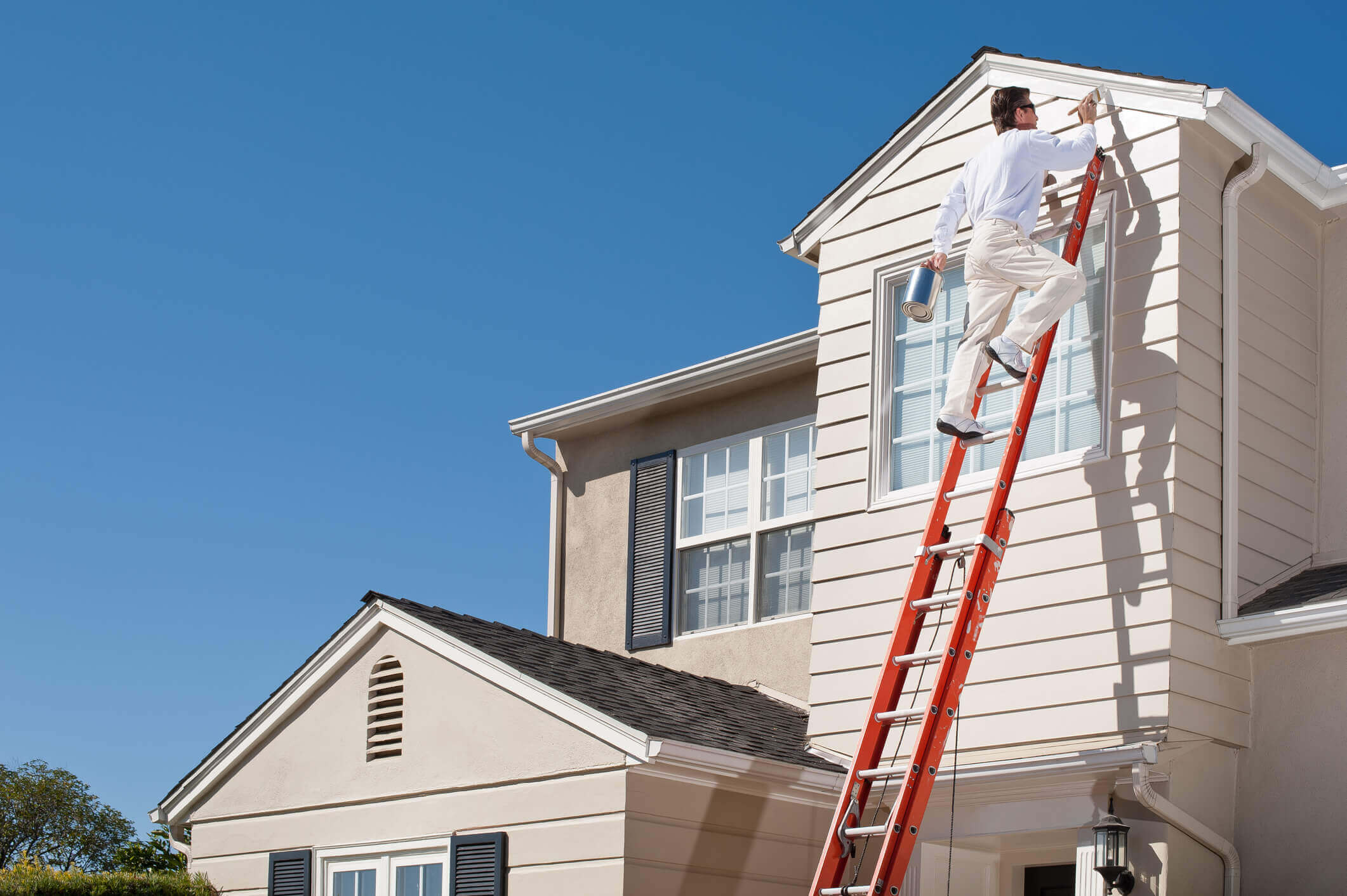 a painter on a ladder doing exterior painting on a home