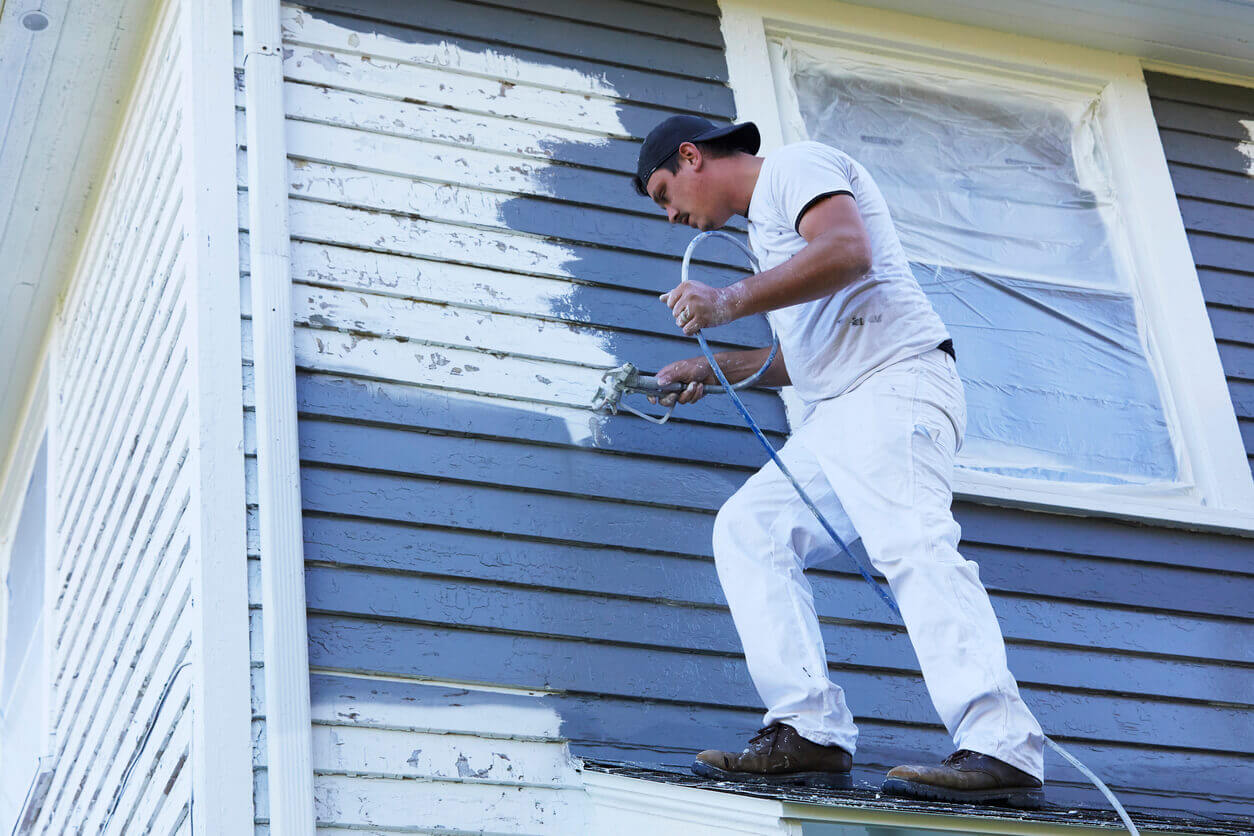 A man painting exterior siding